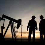 Two oil workers standing near oil drill in predawn light